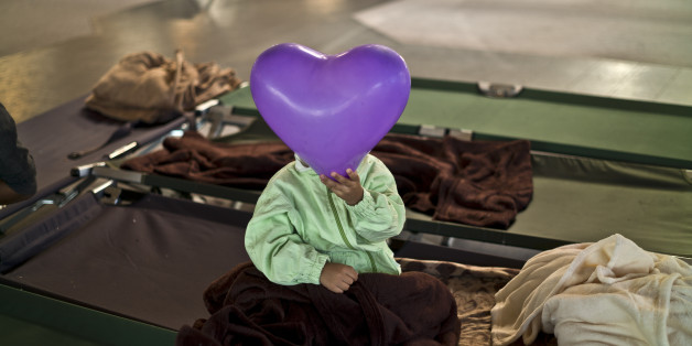 An Afghan refugee child covers his face with a balloon while he and other migrants spent the night in a shelter near Graz, Austria, Tuesday, Sept. 22, 2015. Hungary's prime minister Viktor Orban said that millions of migrants are "laying siege" to the borders of his country and of Europe, putting the continent in danger. (AP Photo/Muhammed Muheisen)