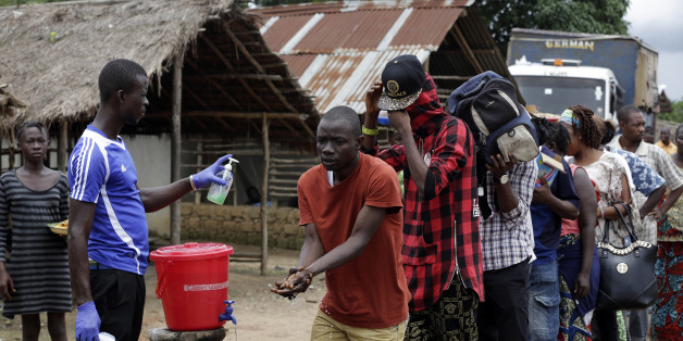 In this photo taken Wednesday, Aug. 12, 2015, a man takes checks people's temperature and helps to wash their hands as they leave Ebola quarantine, after Sierra Leone President Ernest Bai Koroma cut a tape to release the quarantine in the village of Massessehbeh on the outskirts of Freetown, Sierra Leone. Five months after a man traveled to his home village for festivities marking the end of Ramadan, and died suddenly from Ebola, but now President Koroma came to cut down the fencing to mark the formal end of Sierra Leone's largest remaining Ebola quarantine. (AP Photo/Sunday Alamba)