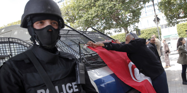 FILE - In this March 20, 2015 file photo, a man places a Tunisian flag onto a police car as a policeman stands guard during a demonstration two days after gunmen attacked the museum and killed scores of people in Tunis, Tunisia. Seven men spent a week in prison on terrorism charges, suffering what they claim was torture under custody, before a judge released them for lack of evidence. But as they stepped out of the courthouse in early August, plainclothes policemen swooped in and spirited them away. (AP Photo/Christophe Ena, File)
