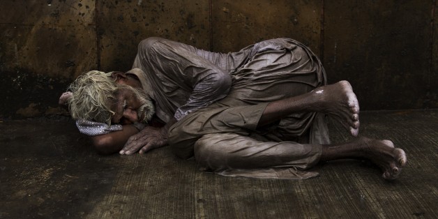 An Indian homeless man tries to sleep on a wet street during monsoon rains in New Delhi, India, Saturday, July 11, 2015. Tens of thousands of impoverished people live on the streets in New Delhi, where they struggle with constant hunger and extreme weather while sleeping nights next to busy intersections and roads. Some make camp in crowded alleyways, in abandoned lots or by garbage dumps. Many come from countryside villages in hopes of finding better economic opportunities in the Indian capital