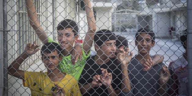 Refugees observe Greece and Austria Prime Ministers from behind a fence at the Moria camp in Lesbos island , Greece, on Tuesday, Oct. 6, 2015. The Austrian Chancellor and the Greek premier visited Lesbos island Tuesday to view first-hand the impact of the refugee crisis and tour facilities set up to handle the thousands of people who arrive daily.(AP Photo/Santi Palacios)