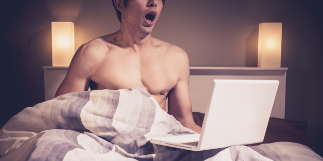 Young man is sitting in bed and watching pornography on his laptop