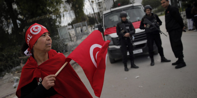 A woman holds a Tunisian flag as policemen stand guard at the National Bardo Museum two days after gunmen attacked the museum and killed scores of people in Tunis, Tunisia, Friday, March 20, 2015. The Islamic State group issued a statement Thursday claiming responsibility for the deadly attack on Tunisia's national museum that killed scores of people, mostly tourists. (AP Photo/Christophe Ena)