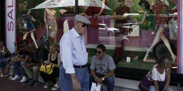 An elderly man passes pedestrians sitting outside a fashion store advertising price discounts in the summer sales in Athens, Greece, on Monday, July 13, 2015. Greece has been in financial limbo since the government missed a payment to the International Monetary Fund and allowed its second rescue package to lapse on June 30. Photographer: Kostas Tsironis/Bloomberg via Getty Images