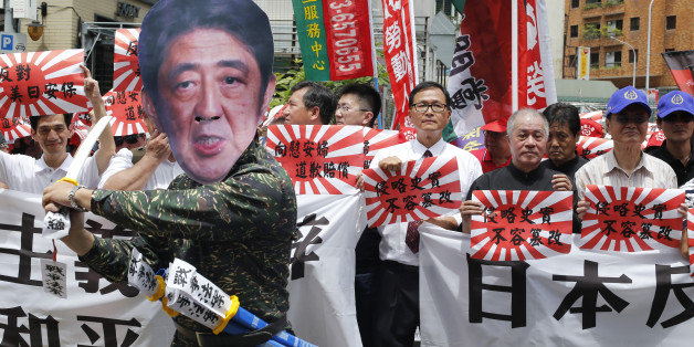 An activist dressed as Japanese Prime Minister Shinzo Abe poses with Japanese military flags reading "Japan must apologize" during an anti-Japan protest outside of the Japan trade office in Taipei, Taiwan, Saturday, Aug. 15, 2015. In a statement marking the anniversary of Japan's surrender, Abe acknowledged Friday that Japan inflicted "immeasurable damage and suffering" on innocent people in World War II, but stopped short of offering his own apology and said future generations of Japanese shoul