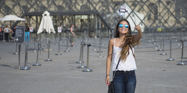 PARIS, FRANCE - AUGUST 06: A tourist takes a selfie using a selfie stick in front of the Louvre Pyramid on August 6, 2015 in Paris, France. Using a selfie stick has become a more and more common place among tourists but a number of high-profile attractions in Paris and other cities have started to ban them over fears of potential damage to exhibits. (Photo by Vanni Bassetti/Getty Images)