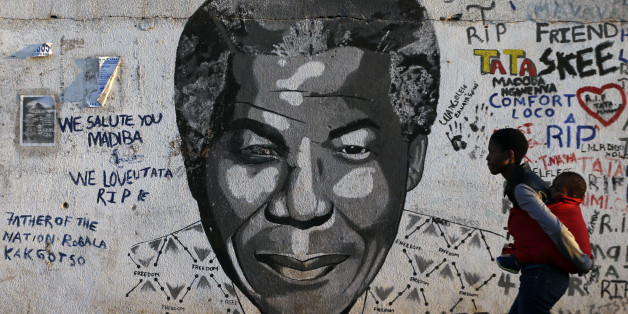 A woman carrying a child on her back walks past a mural showing former South African president Nelson Mandela's face at Katlehong township, 35 km east of Johannesburg, South Africa, Saturday, July 18, 2015. On Mandela Day, people around the world are encouraged to spend at least 67 minutes doing something positive for their communities in honor of the 67 years that the late South African president Nelson Mandela spent fighting for social justice and a free, democratic country. (AP Photo/Themba