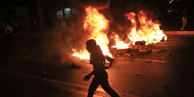 A masked protester runs past garbage bins set on fire by supporters of the pro-Kurdish Peoples's Democratic Party (HDP) in Diyarbakir, in Turkey's predominantly Kurdish southeast, Sunday, Nov. 1, 2015. State-run TRT television says that preliminary results in Turkey's crucial parliamentary election suggest a surprising boost for the ruling party although the result could still change significantly as votes come in from disparate regions of the country. (AP Photo/Lefteris Pitarakis)