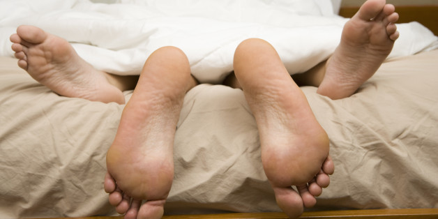 View of feet of couple having sex in bed.