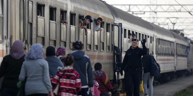 A Croatian police officer helps people board a train at the station in Sid, about 100 km west from Belgrade, Serbia, Tuesday Nov. 3, 2015. Serbia and Croatia have launched a direct train transfer of migrants from one country to another so asylum seekers no longer have to wait long hours outside in the cold. (AP Photo/Darko Vojinovic)