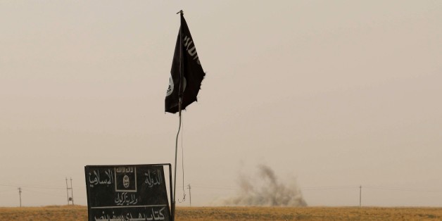 Smoke rises in the distance behind an Islamic State (IS) group flag and banner after Iraqi Kurdish Peshmerga fighters reportedly captured several villages from IS group jihadists in the district of Daquq, south of the northern Iraqi multi-ethnic city of Kirkuk on September 11, 2015. An Iraqi officer said that the operation was launched in the morning with support from international coalition aircraft, and has succeeded in retaking ten villages from IS. AFP PHOTO / MARWAN IBRAHIM (Photo credit should read MARWAN IBRAHIM/AFP/Getty Images)