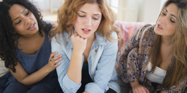 Women comforting sad friend on sofa in living room
