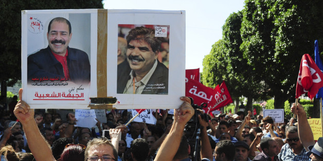 A Tunisian demonstrator holds a poster of slain politicians, lawyer and secular politician Chokri Belaid, left poster, and Mohamed Brahmi, during a march to protest a law offering amnesty for those accused of corruption, in Tunis, Tunisia, Saturday Sept. 12, 2015. The controversial draft law on economic reconciliation is a centerpiece of the new government's program and seeks to boost the economy by clearing cases against businessmen and civil servants accused of corruption. (AP Photo/Riadh Drid