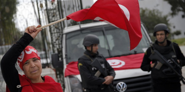 A woman waves the Tunisian flag as policemen stand guard at the National Bardo Museum two days after gunmen attacked the museum and killed scores of people in Tunis, Tunisia, Friday, March 20, 2015. The Islamic State group issued a statement Thursday claiming responsibility for the deadly attack on Tunisia's national museum that killed scores of people, mostly tourists. (AP Photo/Christophe Ena)