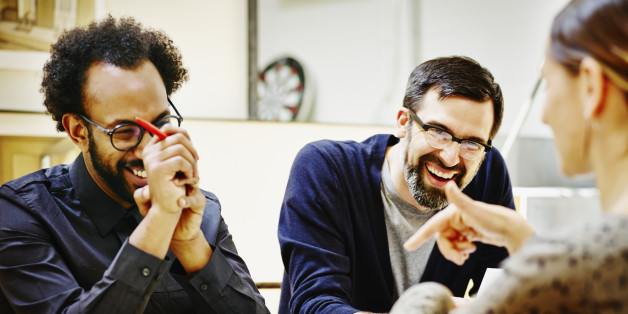 Group of laughing architects discussing project plans at conference table in office
