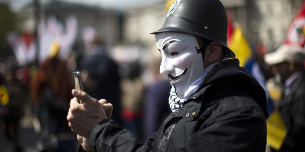A protester wearing a toy British police helmet and an Anonymous mask takes a picture during a rally at the end of a May Day demonstration march in Trafalgar Square in London, Friday, May 1, 2015. Tens of thousands of workers marked May Day in European cities with a mix of anger and gloom over austerity measures imposed by leaders trying to contain the eurozone's intractable debt crisis. (AP Photo/Matt Dunham)