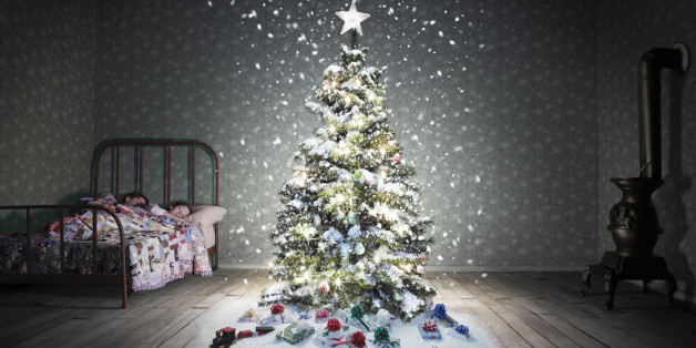 A classic children's bedroom (vintage miniature) with a glowing decorated christmas tree with snow falling. There a two caucasian sisters in the bed that appear to be under 10 years old or younger.