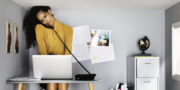 business woman in small office, by her computer, on the phone, looking stressed - her head touching the ceiling
