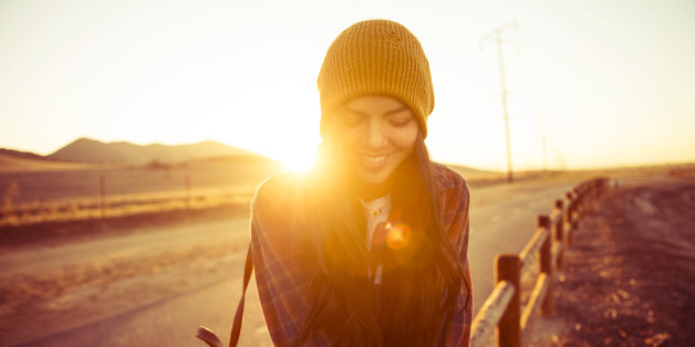 young woman sitting on fence post at sunset