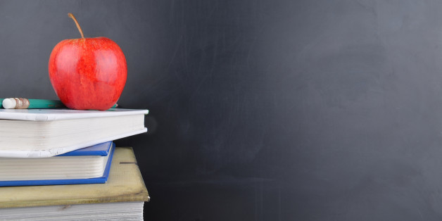 A classroom with a red apple, books and a blackboard with handwriting in white chalk on the board.