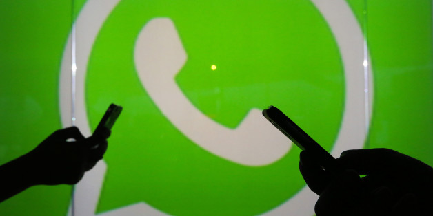 People are seen as silhouettes as they check mobile devices whilst standing against an illuminated wall bearing WhatsApp Inc's logo in this arranged photograph in London, U.K., on Tuesday, Jan. 5, 2016. WhatsApp Inc. offers a cross-platform mobile messaging application that allows users to exchange messages. Photographer: Chris Ratcliffe/Bloomberg via Getty Images