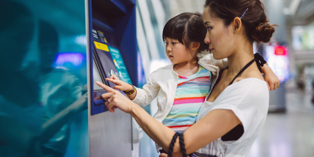 Pretty young mom carrying lovely little girl using an automatic teller machine together in the train station