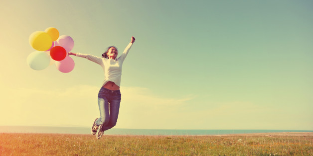 young asian woman running and jumping on green grassland with colored balloons