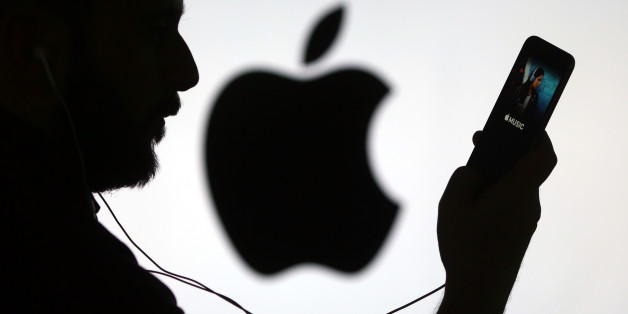 A man checks the Apple Music streaming site using his Apple Inc. iPhone 6s as he stands framed against a wall bearing the Apple logo in this arranged photograph in London, U.K., on Wednesday, Dec. 23, 2015. Beatles songs will now be available around the world on nine streaming services including Apple, Spotify, Deezer and Google Play, the bands record company, Vivendi SAs Universal Music Group, said Wednesday in a statement. Photographer: Chris Ratcliffe/Bloomberg via Getty Images