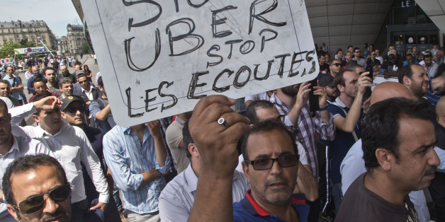 A striking taxi driver holds a placard which read, "Stop Uber, Stop listening," referring to the new US spying report in France, during a taxi drivers demonstration in Paris, France, Thursday, June 25, 2015. French taxis are on strike around the country, snarling traffic in major cities and slowing access to Paris' Charles de Gaulle airport after weeks of rising and sometimes violent tensions over Uber. (AP Photo/Michel Euler)