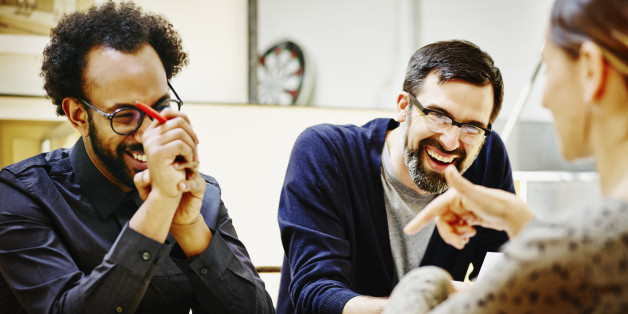 Group of laughing architects discussing project plans at conference table in office