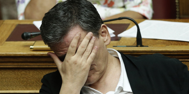 Greek Finance Minister Euclid Tsakalotos covers his face during a parliamentary session in Athens, early Friday, Aug. 14, 2015. The Greek government defended its new bailout program in tumultuous parliamentary sessions as it faced a rebellion in the governing Syriza party ahead of a vote on the deal. (AP Photo/Yannis Liakos)