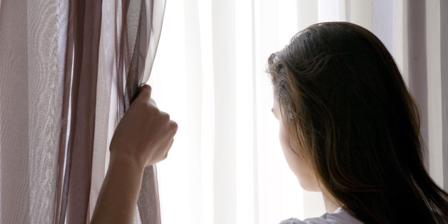 rear view of teenage girl looking through curtain