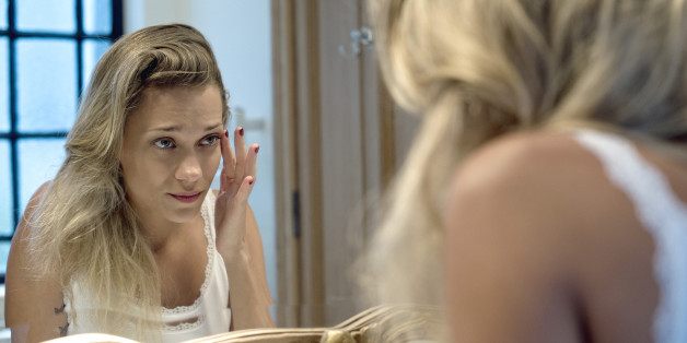 Woman looking bleary-eyed at self in bathroom mirror