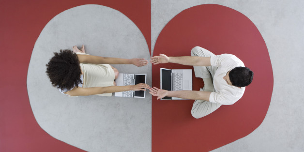 Man and woman sitting with laptops on large heart, arms out, touching hands, overhead view