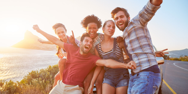 Group Of Friends Standing By Car On Coastal Road At Sunset