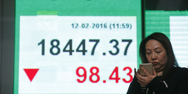 A woman uses her smartphone in front of an electronic board showing the Hong Kong index at a bank in Hong Kong, Friday, Feb. 12, 2016. Japanâs main stock index dived Friday, leading other Asian markets lower, after a sell-off in banking shares roiled investors in the U.S. and Europe. (AP Photo/Kin Cheung)