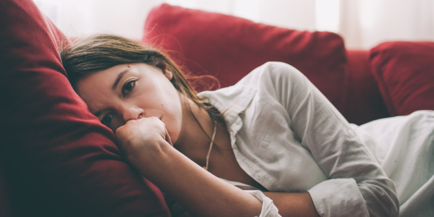 Brunette young woman laying down with tired expression on sofa