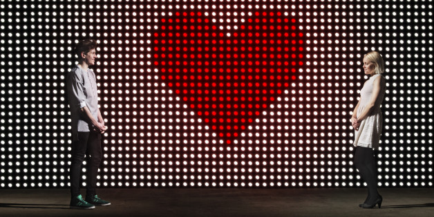 young couple in front of light wall, with huge heart made of red dots, dating