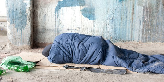 Homeless man sleeping in sleeping bag on cardboard
