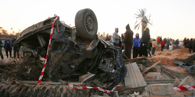 In this Friday, Feb. 19, 2016 photo, people gather by the wreckage of a car, after an air strike on a house and training camp belonging to the Islamic State group, west of Sabratha, Libya. American F-15E fighter-bombers struck an Islamic State militant training camp in rural Libya near the Tunisian border Friday, killing dozens, probably including an IS operative considered responsible for deadly attacks in Tunisia last year, U.S. and local officials said. (AP Photo/Mohamed Ben Khalifa)