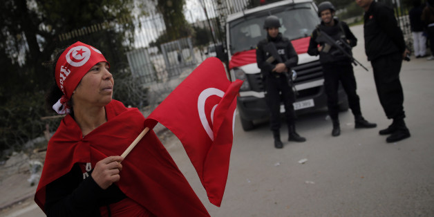 A woman holds a Tunisian flag as policemen stand guard at the National Bardo Museum two days after gunmen attacked the museum and killed scores of people in Tunis, Tunisia, Friday, March 20, 2015. The Islamic State group issued a statement Thursday claiming responsibility for the deadly attack on Tunisia's national museum that killed scores of people, mostly tourists. (AP Photo/Christophe Ena)