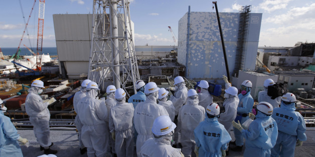 Members of the media tour group, wearing protective suits and masks, receive a briefing from Tokyo Electric Power Co. (TEPCO) employees (in blue) in front of the No. 1, left,and No. 2 reactor buildings at the tsunami-crippled Fukushima Dai-ichi nuclear power plant in Okuma, Fukushima Prefecture, northeastern Japan, Wednesday, Feb. 10, 2016. In one month, Japan is marking the fifth anniversary of a devastating earthquake and tsunami that hit on March 11, 2011 and left nearly 19,000 people dead or