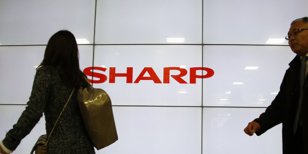 People walk past the log of Sharp Corp. in Tokyo, Thursday, Feb. 25, 2016. Troubled Japanese electronics maker Sharp has agreed to a takeover offer from Taiwanese company Hon Hai, also known as Foxconn, Japanese media reported Thursday. (AP Photo/Shizuo Kambayashi)