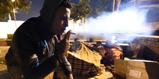 A Moroccan homeless youth smokes as his friends wrapped in blankets attempt to sleep, in a corner of a street in the northeastern coastal city of Tangier, on January 28, 2016.
Having left their homes due to precarious social circumstances, some of these children attempt to travel to Europe by jumping on the back of a truck or a bus at the port of the city, in hope of finding a better life elsewhere. Drug addiction is very common among street children who commonly sniff glue and other chemicals to help them bear hunger and cold. / AFP / FADEL SENNA (Photo credit should read FADEL SENNA/AFP/Getty Images)