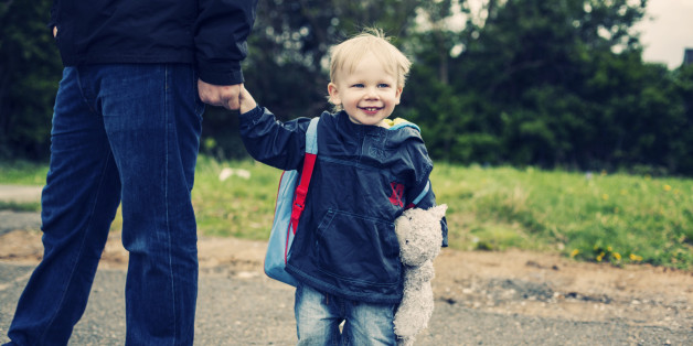 Little boy carrying teddy bear and walking to nursery school with his daddy.