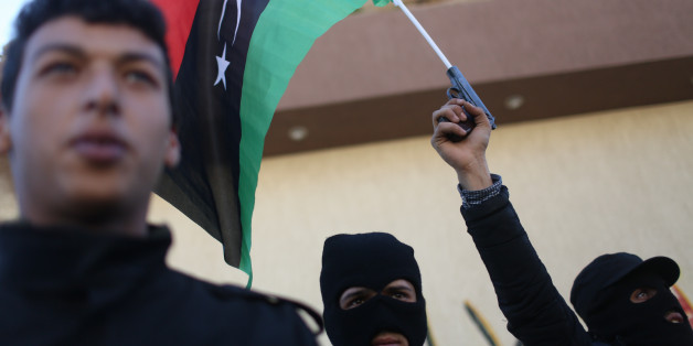 Libyan security forces stand in front of the security headquarters, one showing his weapon with a Libyan flag, in the western city of Sabratha, Libya, Saturday, Feb. 20, 2016. American fighter-bombers struck an Islamic State militant training camp in rural Libya near Sabratha Friday, killing dozens. Serbian officials say two Serbian embassy staffers who had been held hostage since November are believed to have been killed in the airstrikes. Washington and its European allies are seeking to end t