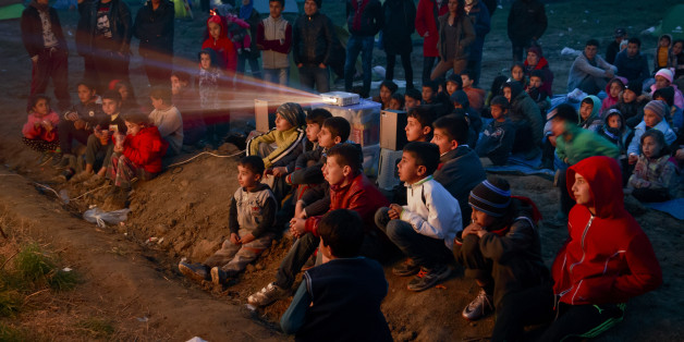Children watch a cartoon movie in a field at the northern Greek border station of Idomeni, Saturday, March 5, 2016. The regional governor of the Greek region of Central Macedonia called on the Greek government Saturday to declare a state of emergency for the area surrounding the Idomeni border crossing saying that up to 14,000 people are trapped in Idomeni, while another 6,000-7,000 are being housed in refugee camps around the region, meaning the area was handling about 60 percent of the total number in the country. (AP Photo/Vadim Ghirda)