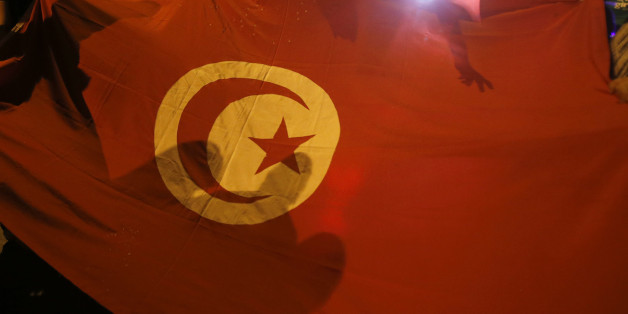 People carry a Tunisian flag during an protest against terrorism in Sousse, Tunisia, Saturday, June 27, 2015. Tunisia's postcard destination for tourists is reeling from the terror that blighted another day of play at the Mediterranean seaside resort of Sousse. A man armed with a Kalashnikov and grenades gunned down tourists on a private beach Friday, and then moved methodically through the grounds of a luxury hotel â to the swimming pool, reception area and offices. (AP Photo/Darko Vojinovic)
