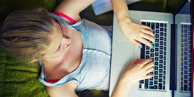 Teenage girl sitting on a sofa, working with a notebook.