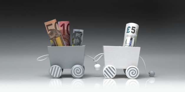 Detail of a toy train, consisting of two wooden wagons. The wagons are connected between them and they are shot on a gradient background. One wagon is pulling the other. The wagons are carrying euros and pounds in banknotes. The photograph was shot in a studio and its frame is horizontal.